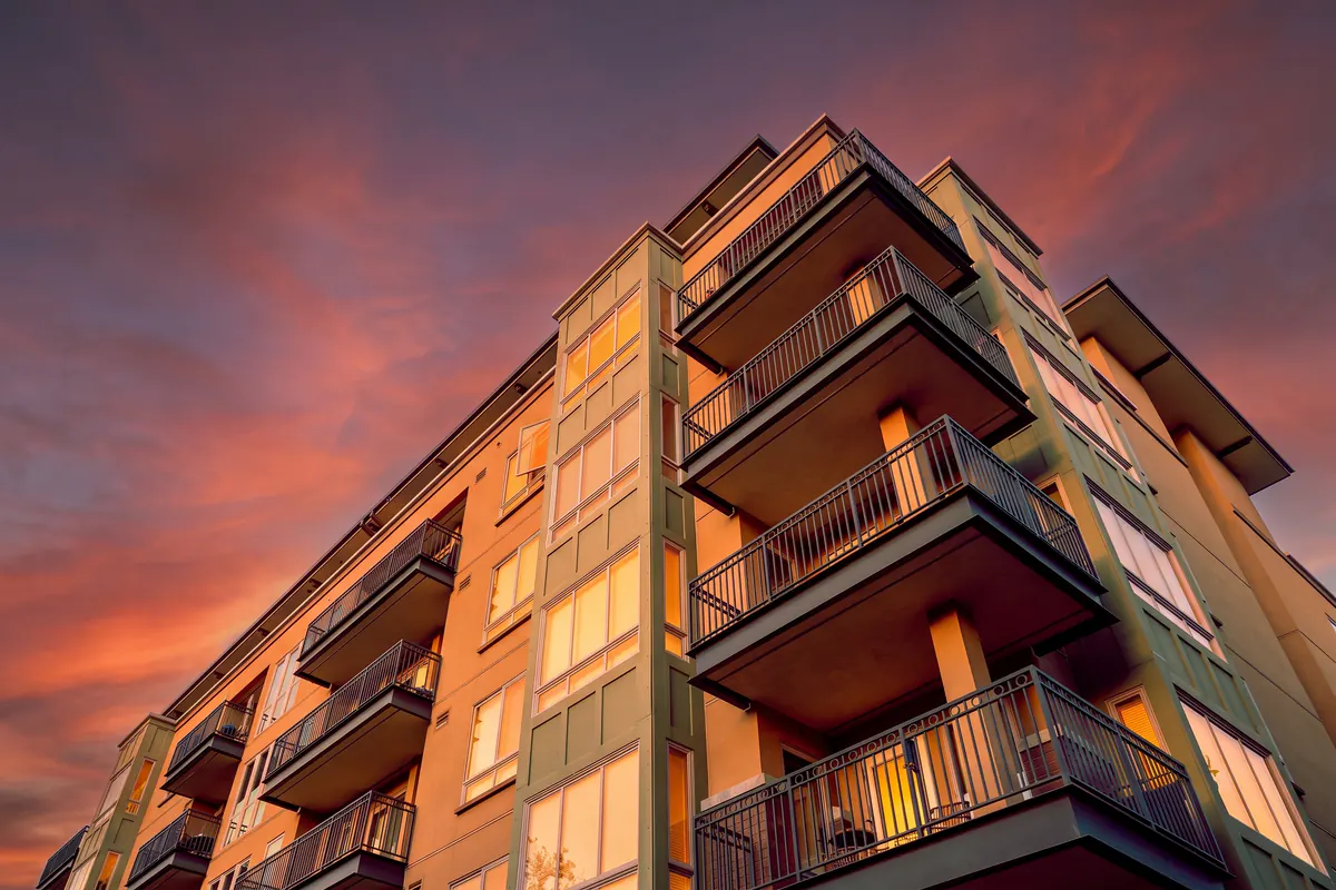 Retouche IA jour-crépuscule à 19:00 : immeuble d'habitation de hauteur moyenne avec balcons
